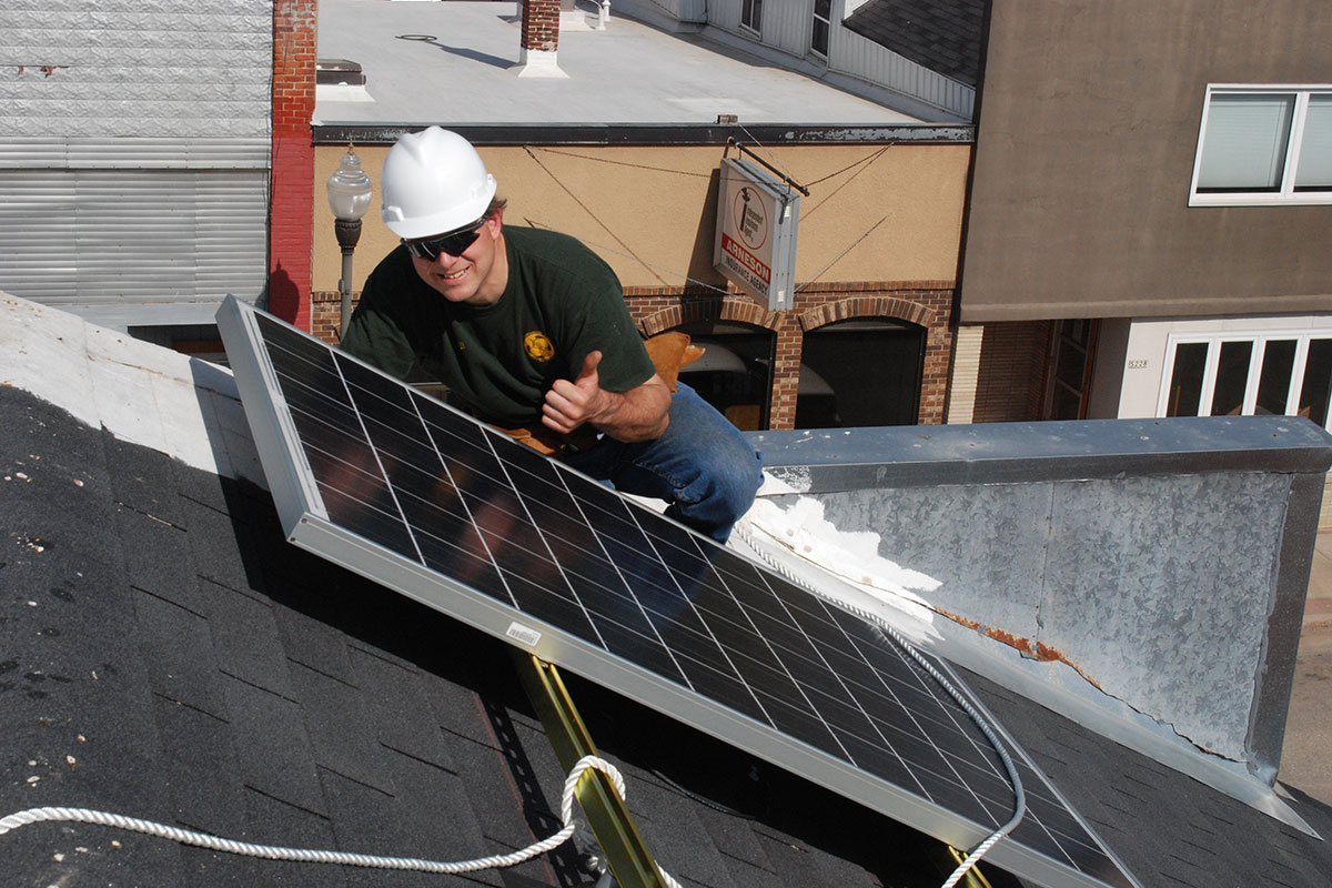 solar installer in a white hard hat giving a thumbs up on a roof with a solar panel