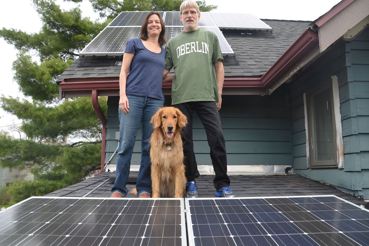 Toland and Passos standing on roof with solar panels and golden retriever