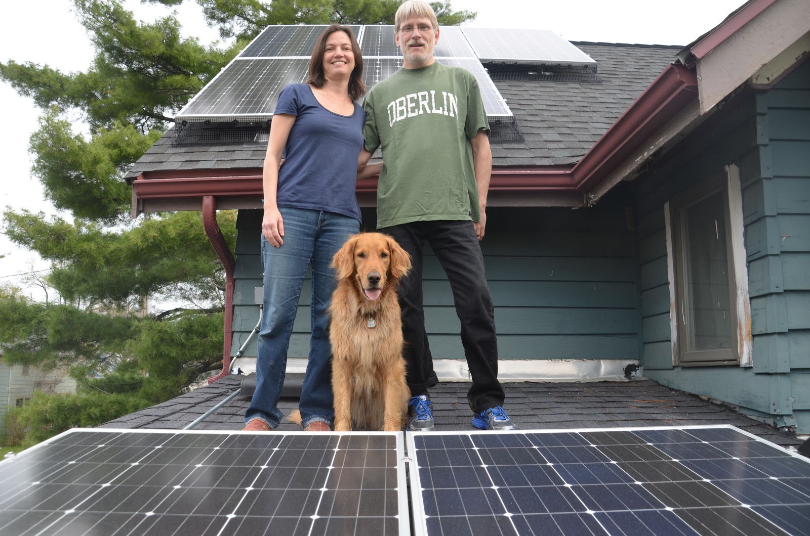 Toland and Passos standing on roof with solar panels and golden retriever